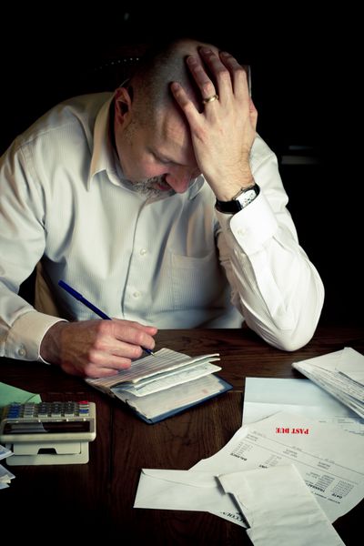 مردی استرس‌زده با دسته چک که در حین کار بر روی امور مالی خانه مشکل دارد