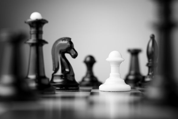 پیاده سفید که توسط مهره های شطرنج سیاه روی یک صفحه شطرنج احاطه شده است