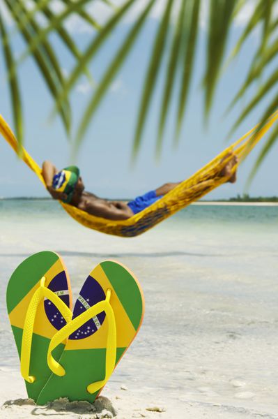 مردی در بانوج بر فراز دریا استراحت می‌کند و دمپایی پرچم برزیل خود را روی شن‌ها می‌گذارد