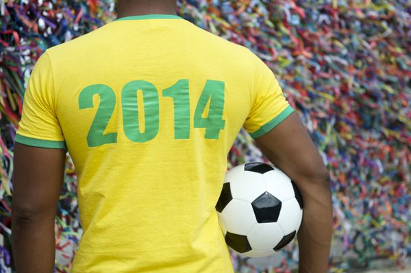 بازیکن فوتبال برزیل 2014 با فوتبال در مقابل دیوار روبان های آرزوهای رنگارنگ لمبرانکا در سالوادور باهیا برزیل ایستاده است