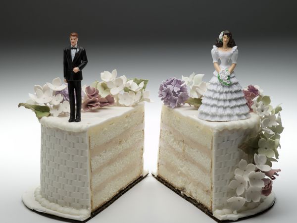 مجسمه های عروس و داماد که روی دو برش جدا شده از کیک عروسی ایستاده اند