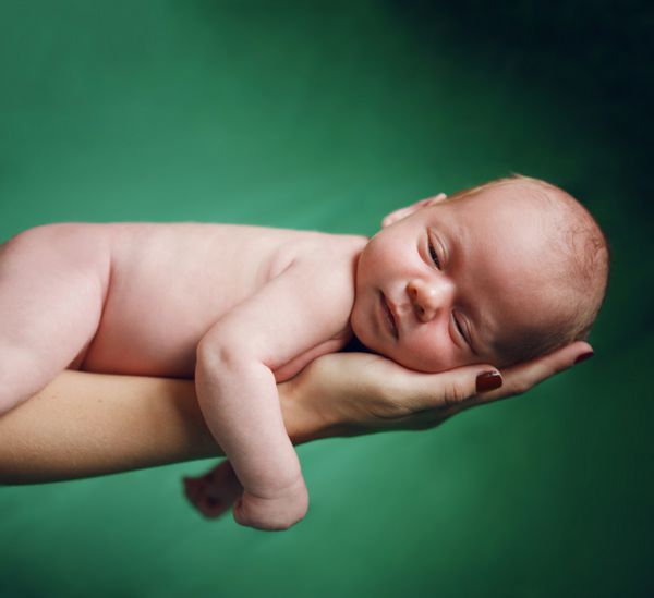 نوزاد زیبای تازه متولد شده روی دست مادر تکیه داده است
