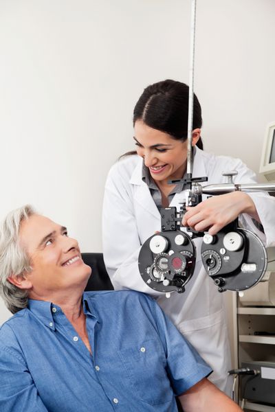 متخصص چشم مراقبت قبل از انجام آزمایش چشم با فوروپتر به بیمار بالغ لبخند می زند