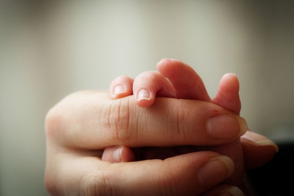 نوزادی که انگشت مادرش را در دست گرفته است تمرکز انتخابی