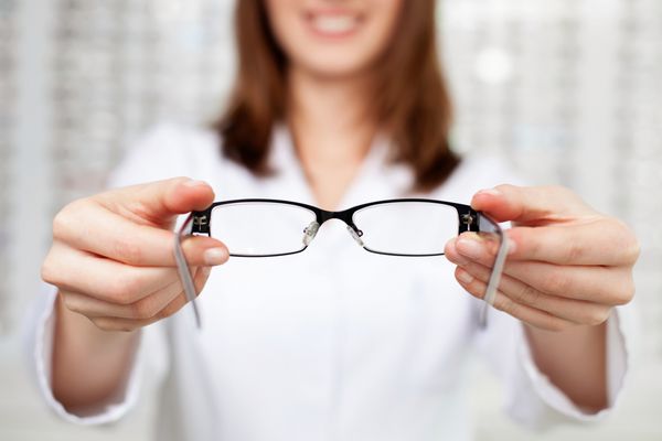 نمای نزدیک از بینایی‌سنج بینایی‌شناس که عینک را امتحان می‌کند