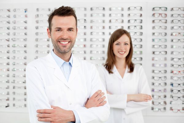 دو بینایی‌شناس شاد که در فروشگاه بینایی‌سنجی ایستاده‌اند