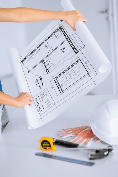 مفهوم معماری و بازسازی خانه - زن با طرح اولیه خط کش انعطاف پذیر کلاه ایمنی و چکش