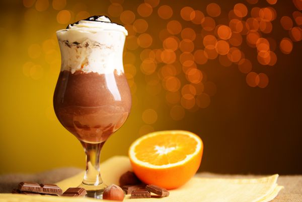 دسر خوش طعم با شکلات خامه و سس پرتقال روی میز چوبی در زمینه نور