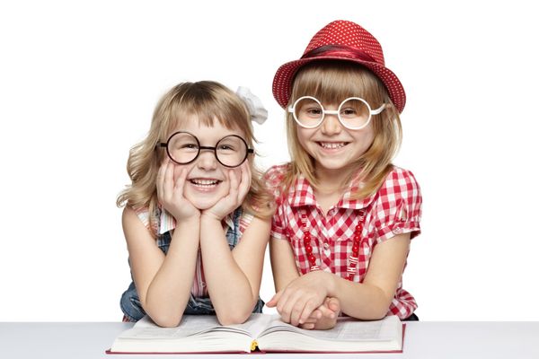 دو دختر کوچک با عینک های خنده دار در حال خواندن کتاب روی پس زمینه سفید