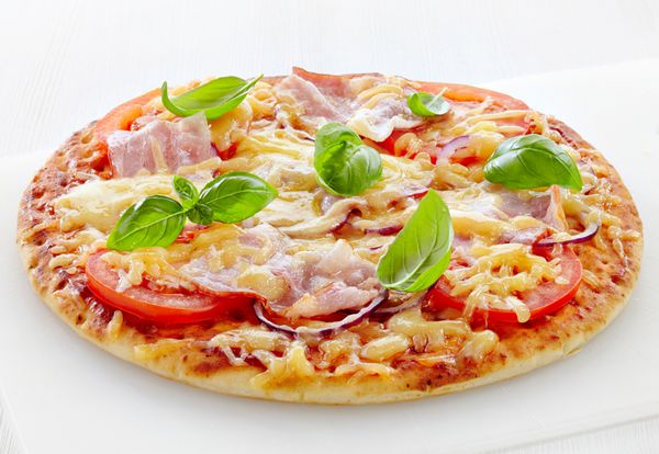 پیتزا با بیکن و گوجه فرنگی روی تخته برش سفید