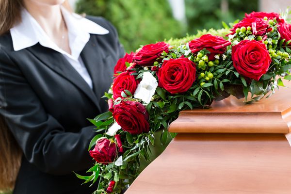 زن عزادار در مراسم تشییع جنازه با گل رز قرمز در تابوت یا تابوت ایستاده است