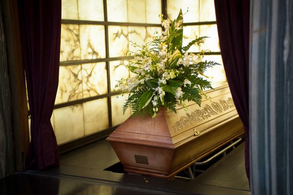 تابوت چوبی با گل های تشییع جنازه در کوره مرده سوز