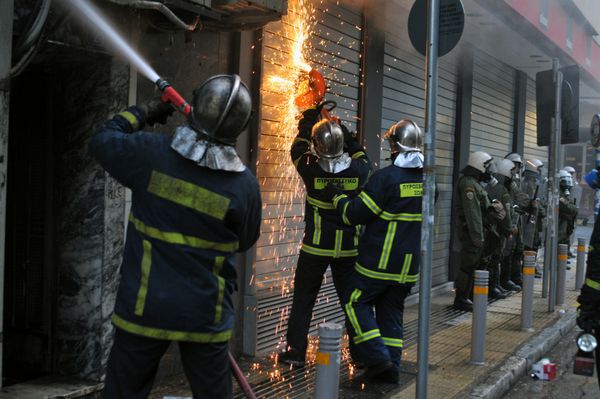 آتن-یونان - دسامبر 20 آتش نشانان تحت محافظت پلیس ضد شورش تلاش می کنند تا فروشگاه در حال سوختن به نام plaisio را در پی یک آتش سوزی در جریان شورش های جمعی در مرکز آتن 20 دسامبر 2008 خاموش کنند