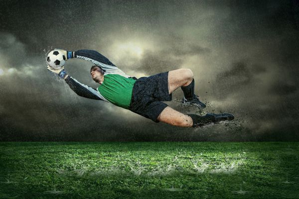 بازیکن فوتبال با توپ در حال عمل زیر باران در فضای باز