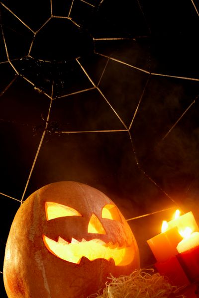 تصویر کدو تنبل هالووین با شمع های در حال سوختن و تار عنکبوت با عنکبوت های نزدیک
