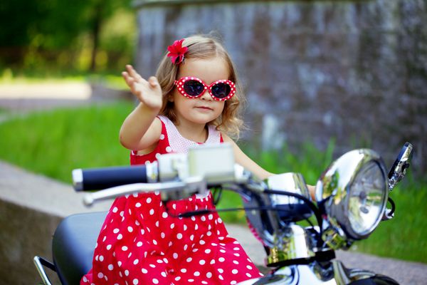 دختر کوچک زیبا با لباس قرمز روی موتور سیکلت