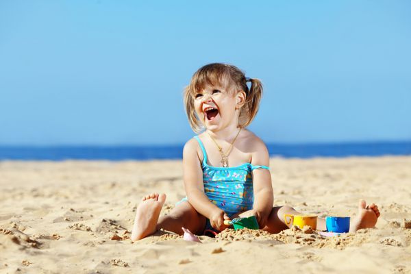 کودک شاد در حال بازی با شن و ماسه در ساحل در تابستان