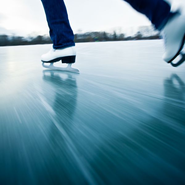 اسکیت روی یخ زن جوان در یک روز سرد زمستانی در فضای باز روی حوض - جزئیات پاها موشن تاری برای انتقال سرعت استفاده می شود تصویر رنگی