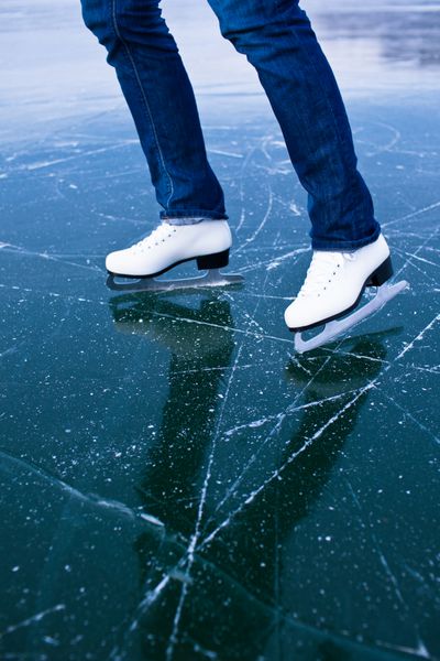 اسکیت روی یخ زن جوان در یک روز سرد زمستانی در فضای باز روی حوضچه - جزئیات پاها