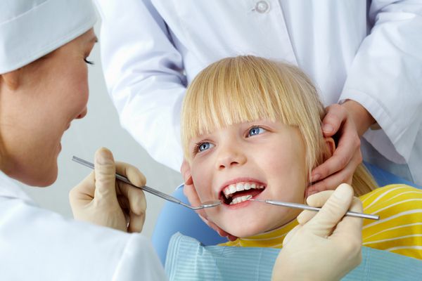 تصویر دختر بچه ای که دندان هایش را توسط پزشک و دستیار معاینه می کند