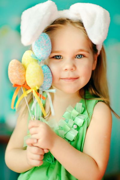 پرتره دختر کوچولوی بامزه ای که در گوش های اسم حیوان دست اموز عید پاک پوشیده است و تخم مرغ های رنگارنگ در دست دارد
