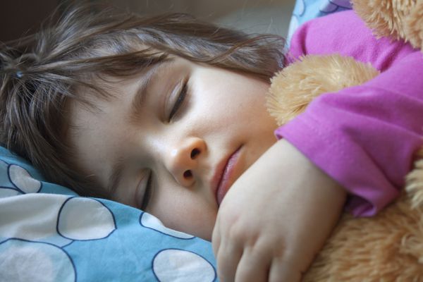 کودک خوابیده در تختش با خرس عروسکی
