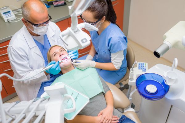 دندانپزشک و پرستار حرفه ای دندان های بیمار زن جراحی دندان را بررسی می کنند