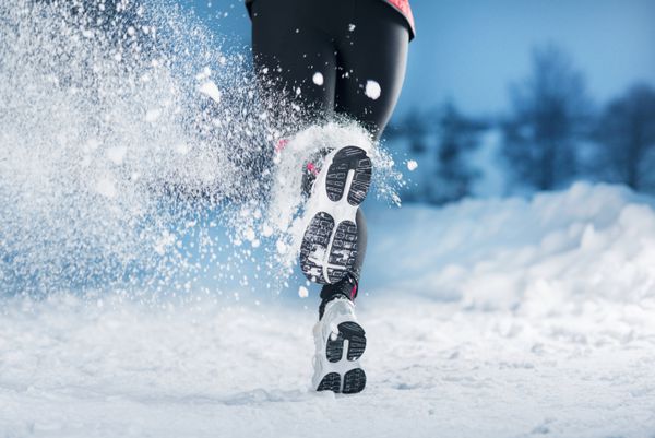 زن ورزشکار در حال دویدن در حین تمرین زمستانی در بیرون در هوای سرد برفی است