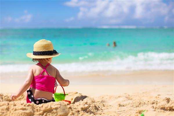 دختر کوچولوی شایان ستایش با لباس شنا و کلاه در ساحل استوایی