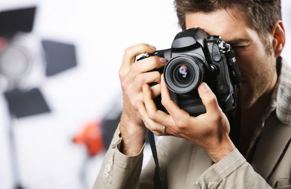 مرد جوانی که با دوربین دیجیتال حرفه ای عکس می گیرد روی دست و لنز تمرکز می کند