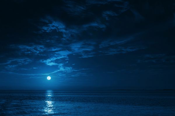 این تصویر تصویری از اقیانوس مهتابی آبی عمیق در شب با امواج آرام پس‌زمینه سفری عالی برای هر منطقه ساحلی یا تعطیلات ایجاد می‌کند