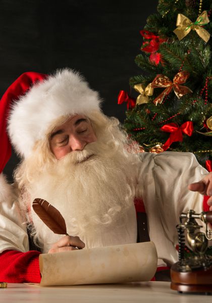 پرتره بابا نوئل در حال پاسخ دادن به نامه های کریسمس با استفاده از ابزارهای قدیمی - رول کاغذ قلم پر جوهر تلفن رترو چوبی