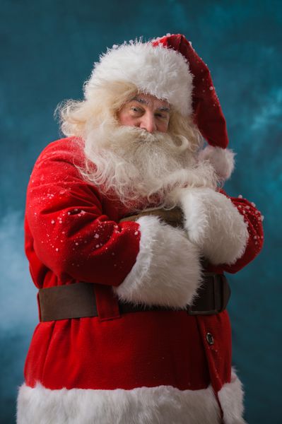 بابا نوئل در فضای باز در هنگام بارش برف در قطب شمال با دستان بسته ایستاده است