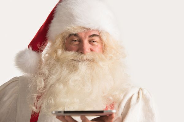 پرتره بابا نوئل خوشحال که رایانه لوحی را در دستان خود گرفته و به دوربین نگاه می کند