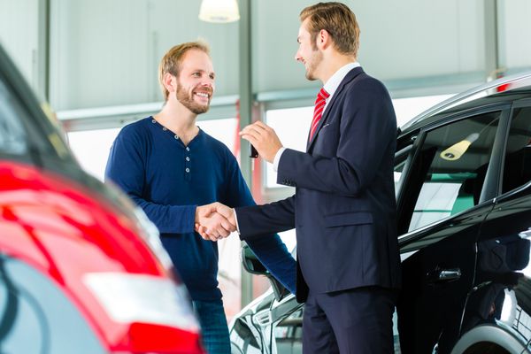 فروشنده یا فروشنده خودرو و مشتری در نمایندگی خودرو دست می دهند کلید ماشین را تحویل می دهند و خرید خودرو یا ماشین نو را مهر می کنند