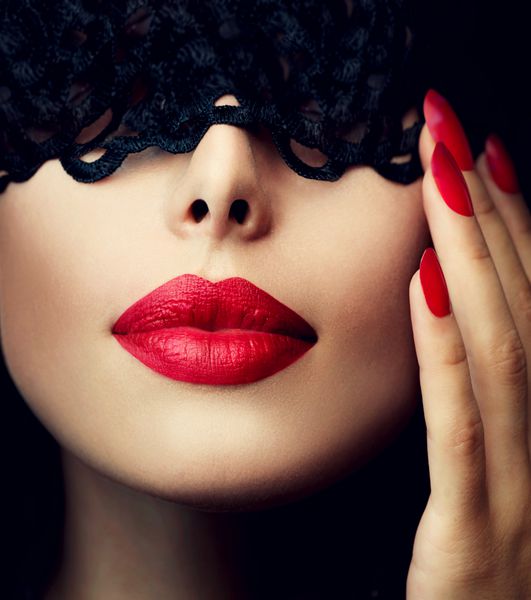 زن زیبا با ماسک توری سیاه روی چشم هایش نمای قرمز لب ها و ناخن ها