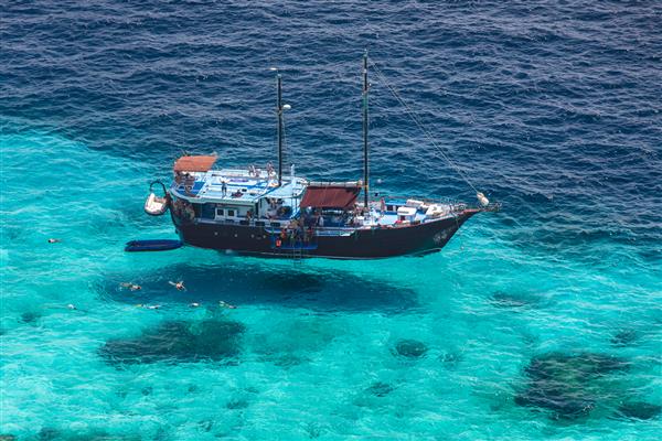 نمای هوایی جزیره گرمسیری دریای آبی شفاف و یک قایق توریستی در یک روز آفتابی