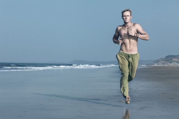 مرد جوان ورزشکار صبح زود در ساحل می دود