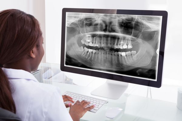 نمای عقب دندانپزشک زن در حال معاینه اشعه ایکس فک روی کامپیوتر در کلینیک