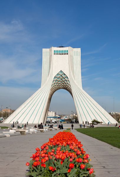 تهران - 1 آوریل بنای یادبود آزادی پشت لاله های قرمز در برابر آسمان آبی در 1 آوریل 2014 در تهران ایران بنای یادبود آزادی مشهورترین بنای تاریخی تهران است که در مرکز میدان آزادی قرار دارد