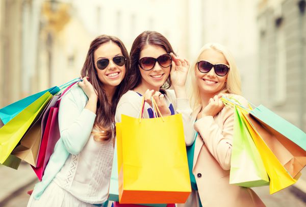 خرید فروش مردم شاد و مفهوم گردشگری - سه دختر زیبا با عینک آفتابی با کیسه های خرید در ctiy