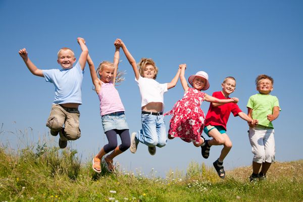 گروه بچه های شادی که روی چمنزار تابستانی مقابل آسمان آبی می پرند