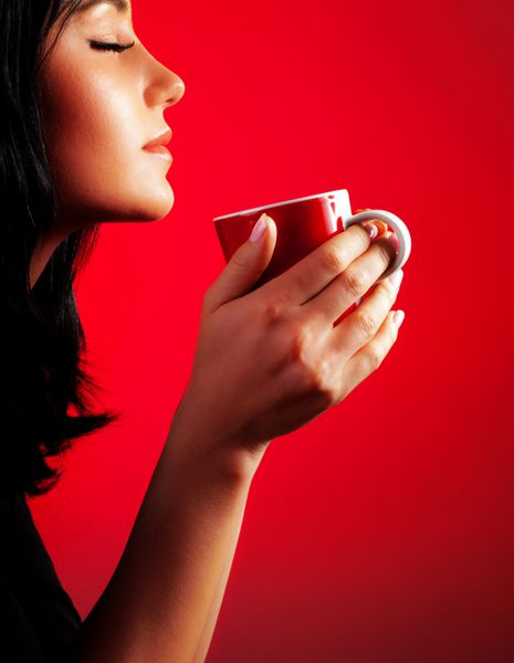 بانوی زیبا قهوه می نوشد سبزه از فنجان شکلات داغ لذت می برد نمای جانبی دختر ناز جدا شده در زمینه قرمز پرتره زن با چای صبح زن زرق و برق دار فنجان کاپوچینو در دست دارد