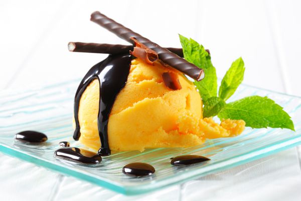 یک قاشق بستنی زرد با سس شکلات و چوب نعناع