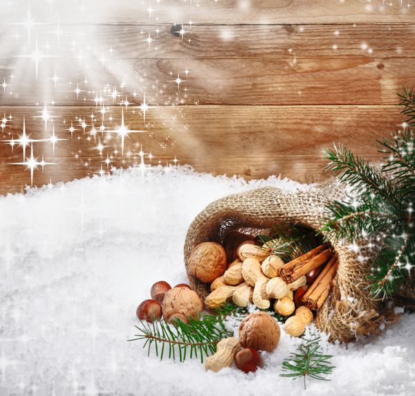 آجیل و ادویه جشن کریسمس که از یک کیسه کریسمس روی برف تازه زمستانی می‌چرخد همراه با نور خورشید که دانه‌های برف و کپی‌های برف را چشمک می‌زند