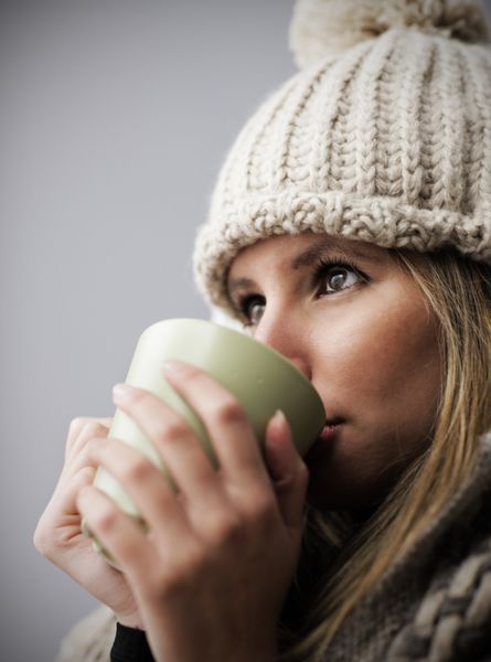 زن جوانی که لباس زمستانی پوشیده و نوشیدنی گرم دارد