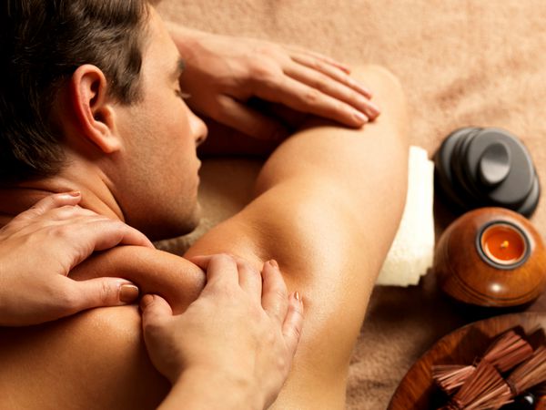 ماساژور در حال انجام ماساژ روی بدن مرد در سالن آبگرم مفهوم درمان زیبایی