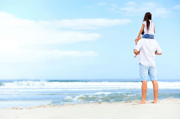 پدر دوست داشتنی با دختری روی شانه که بی خیال و شاد در ساحل قدم می زند