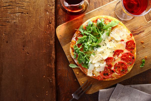 پیتزای سه رنگ ایتالیایی وطنی با نوارهای قرمز سفید و سبز در رنگ‌های پرچم ملی که از گوجه‌فرنگی پنیر و برگ‌های موشک تازه برای رویه روی میز چوبی استفاده می‌شود