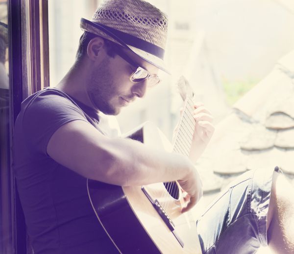 مرد جوانی که روی پنجره نشسته و گیتار می نوازد